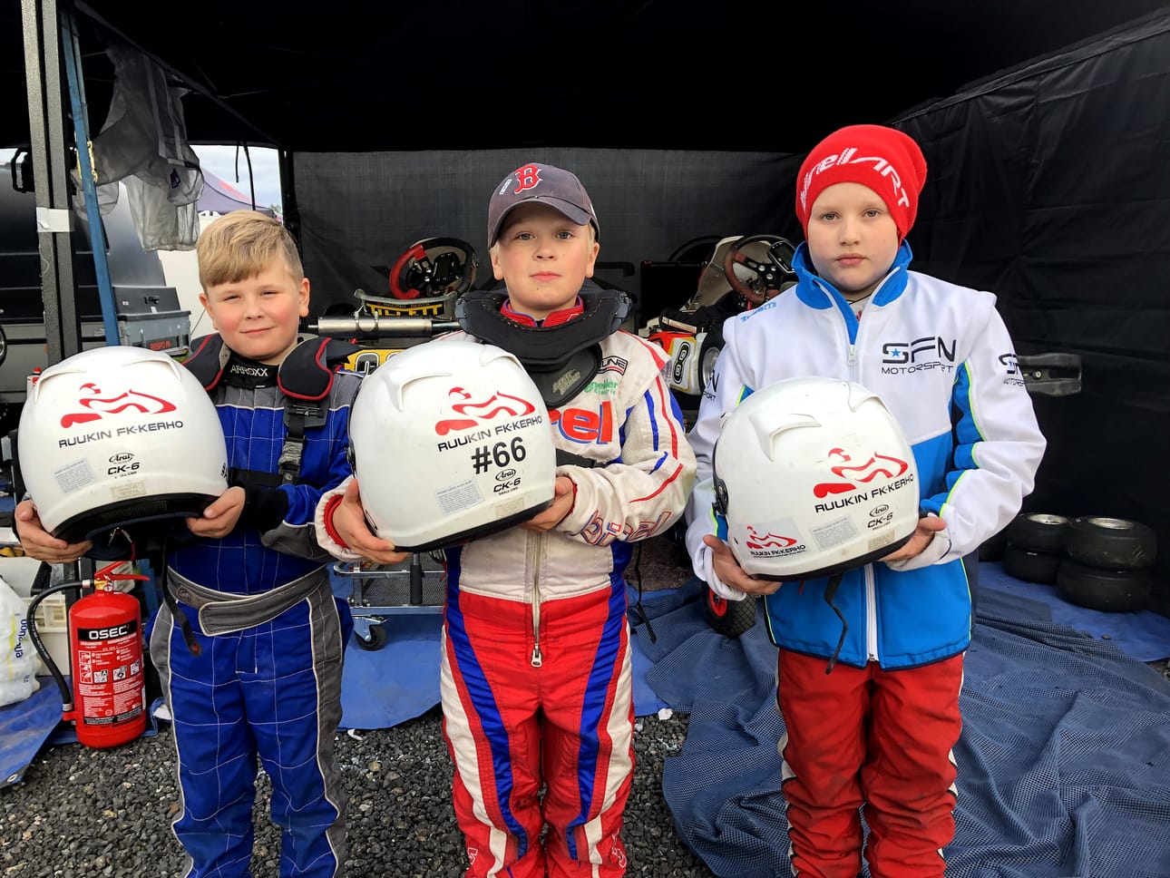 Cadet-kuskit Aleksi Raiski, Miko Haaranen, Eemil-Eepi Mäki-Uuro esittelevät kypäriään, joissa komeilevat Ruukin FK Racing Team logot.