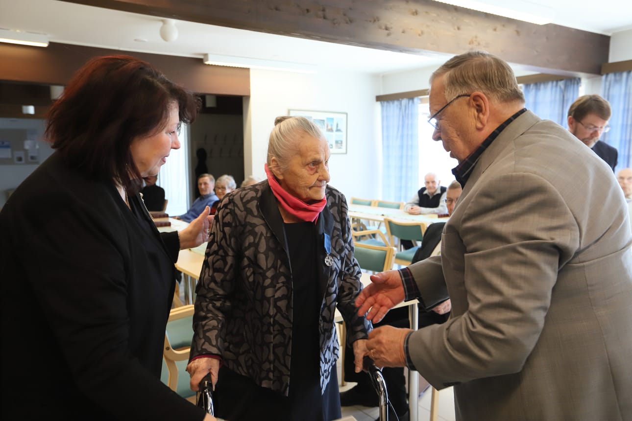 Elma Palokari sai Suomen Valkoisen Ruusun ritarikunnan 1 luokan mitalin. Mitalista onnittelee Matti Mikkola ja saattajana Raili Palokari.