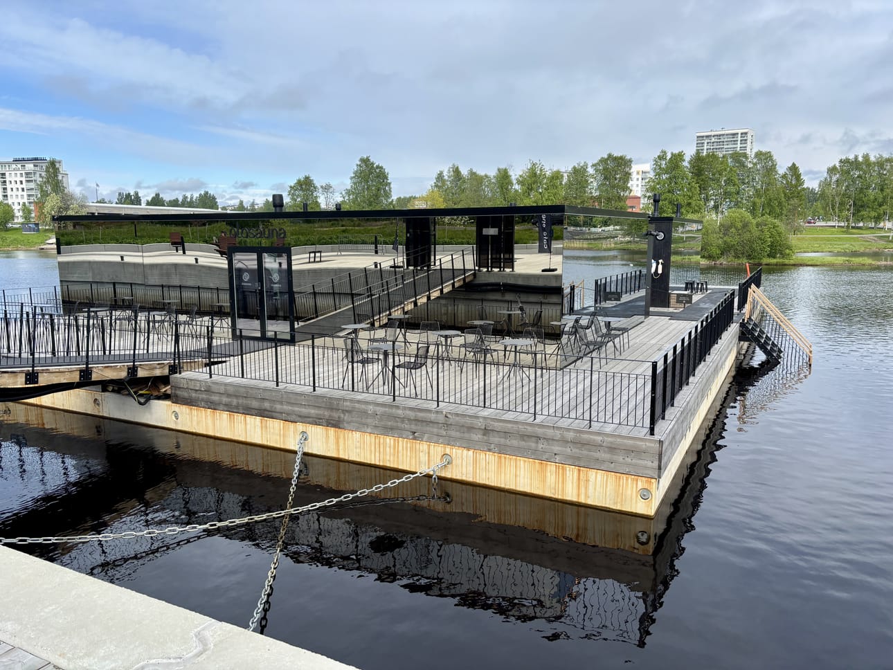 Olosauna kelluu Vaakunakylän edustalla. Kahvilan terassi levittäytyy rakennuksen eteen.