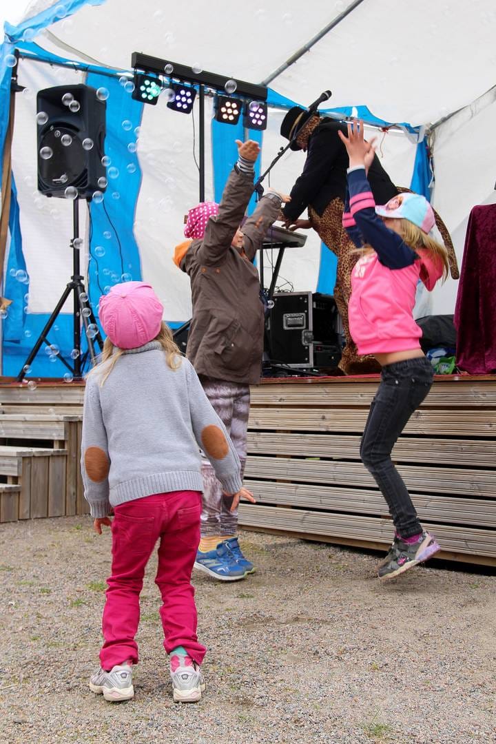 Tytöt tanssivat saippuakuplien keskellä. Takana musisoi Pressan katti.