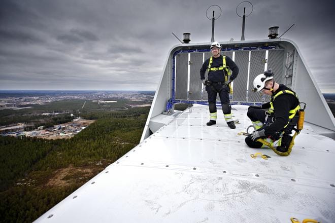 Kouluttaja, huoltoteknikko Toni Keisala ja huoltoteknikko Juuso Kaari työpaikkansa huipulla. Takana näkyy voimalan nestejäähdytysjärjestelmän lauhduttimet sekä lentokoneita varoittavat vilkkuvalot. Voimalan putoamisvaarallisilla alueilla liikuttaessa käytetään valjaita, joiden pitää olla kiinnitettynä aina vähintään yhdellä klipsillä. KUVAT: TOMI KOSONEN