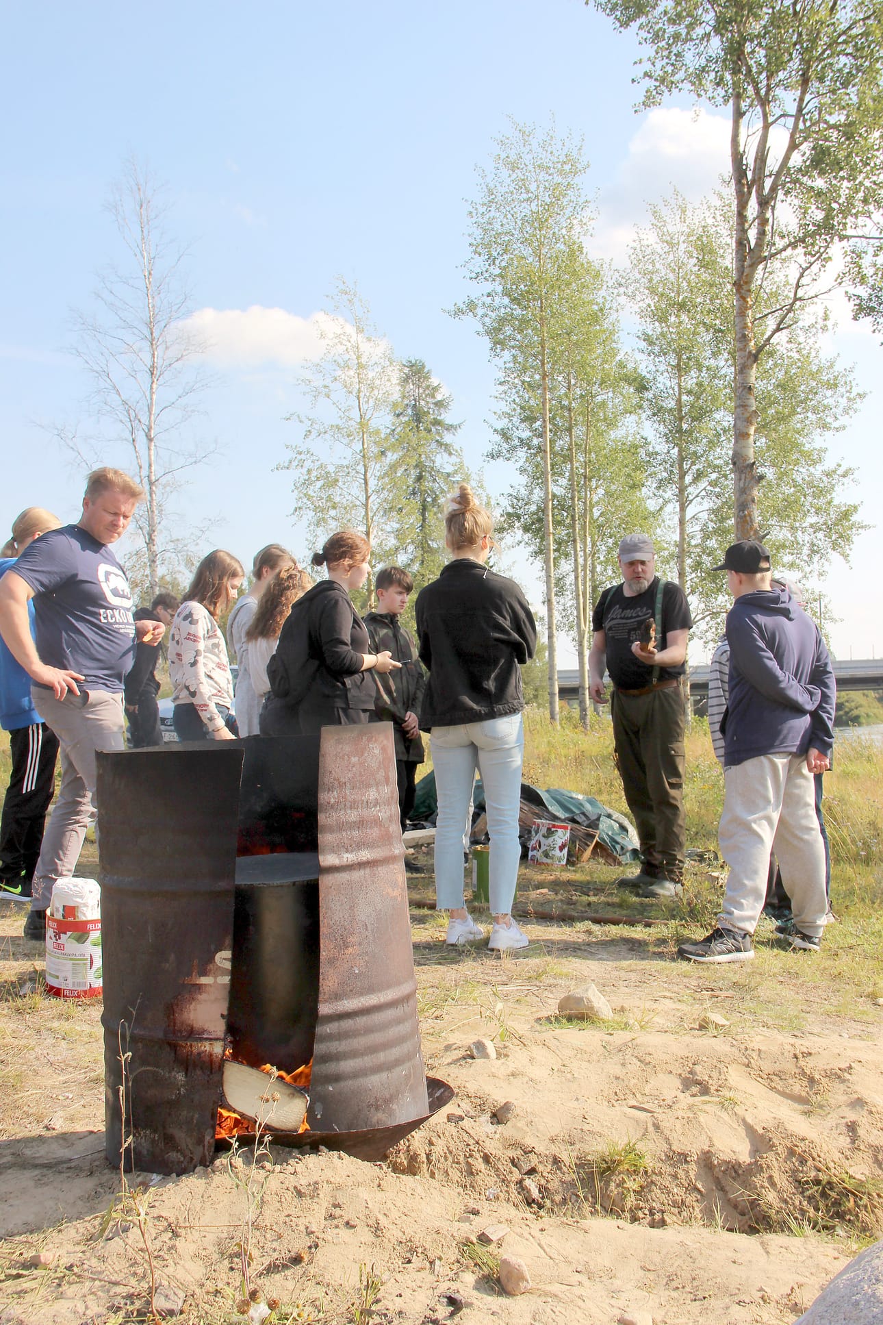 Terva tuoksui Iijoen rannassa Pudasjärvi-päivänä. Tehtaan toimintaa uteliaille esittelivät Hirsikampuksen Jopo-luokan opettaja Ville Eroma ja ohjaaja Janne Laakkonen.
