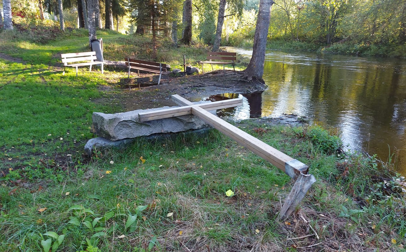Pappilanniemen ranta on kesäisin suosittu uimapaikka. Seurakunnassa on totuttu siihen, että nuoriso käyttää penkkejä hyppyalustoina, mutta nyt loppukesästä penkkejä ja osia nuotiotelineistä on nakeltu lähes tulvivaan jokeen. Etualalla kaadettu, yli kaksimetrinen risti.