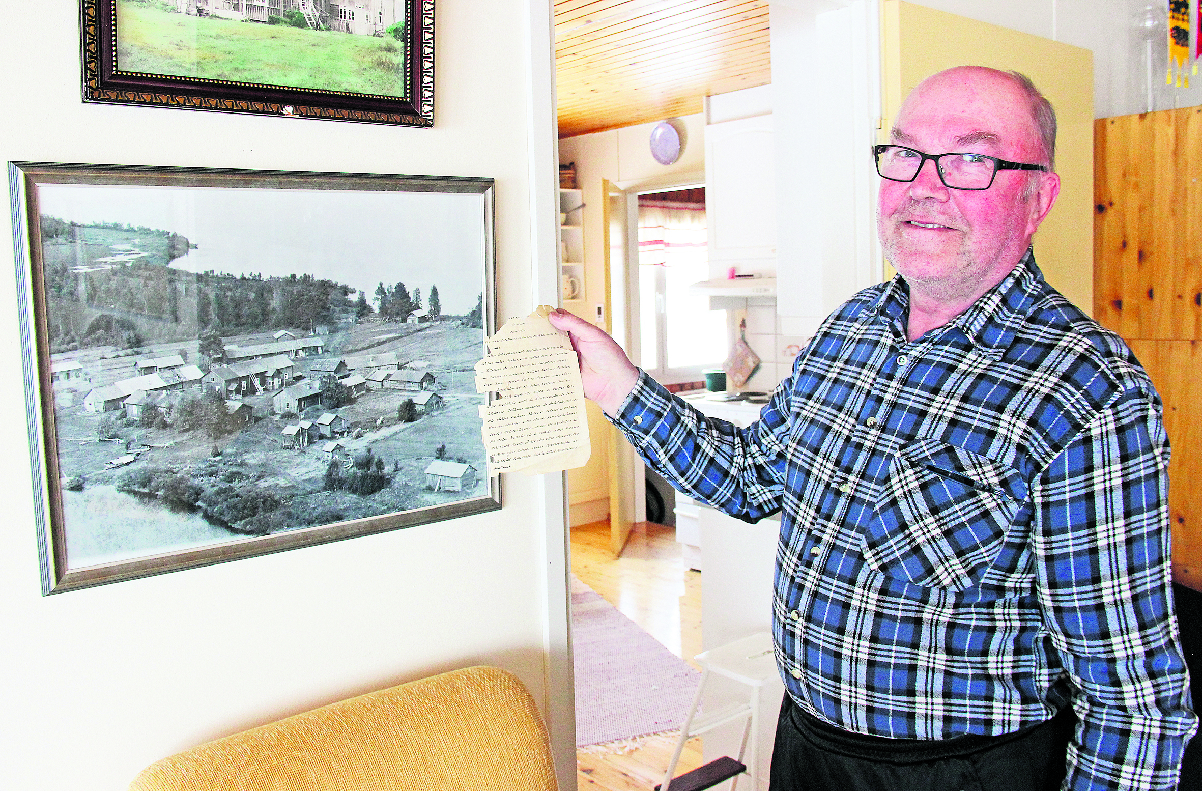Pekka Jussila näyttää vuosikymmenet tallessa ollutta paperinpalaa. Seinällä on kuva Liikasen kartanosta.