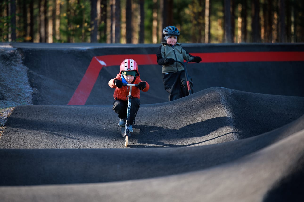 Liam ja Emil Lampi hurjastelevat pumptrack-radalla. Heidän mielestään scoottaamisessa parasta on radan kummut, joista nousee ilmaan.