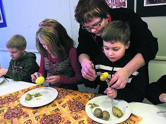 Pohjois-Pohjanmaan Martat ry:n neuvoja Marja-Leena Pirkola opasti ekaluokkalaista Vili Tuppuraista perunan kuorimisessa. Veera Lakso ja Julius Sarajärvi (vas.) keskittyvät omiin perunoihinsa.