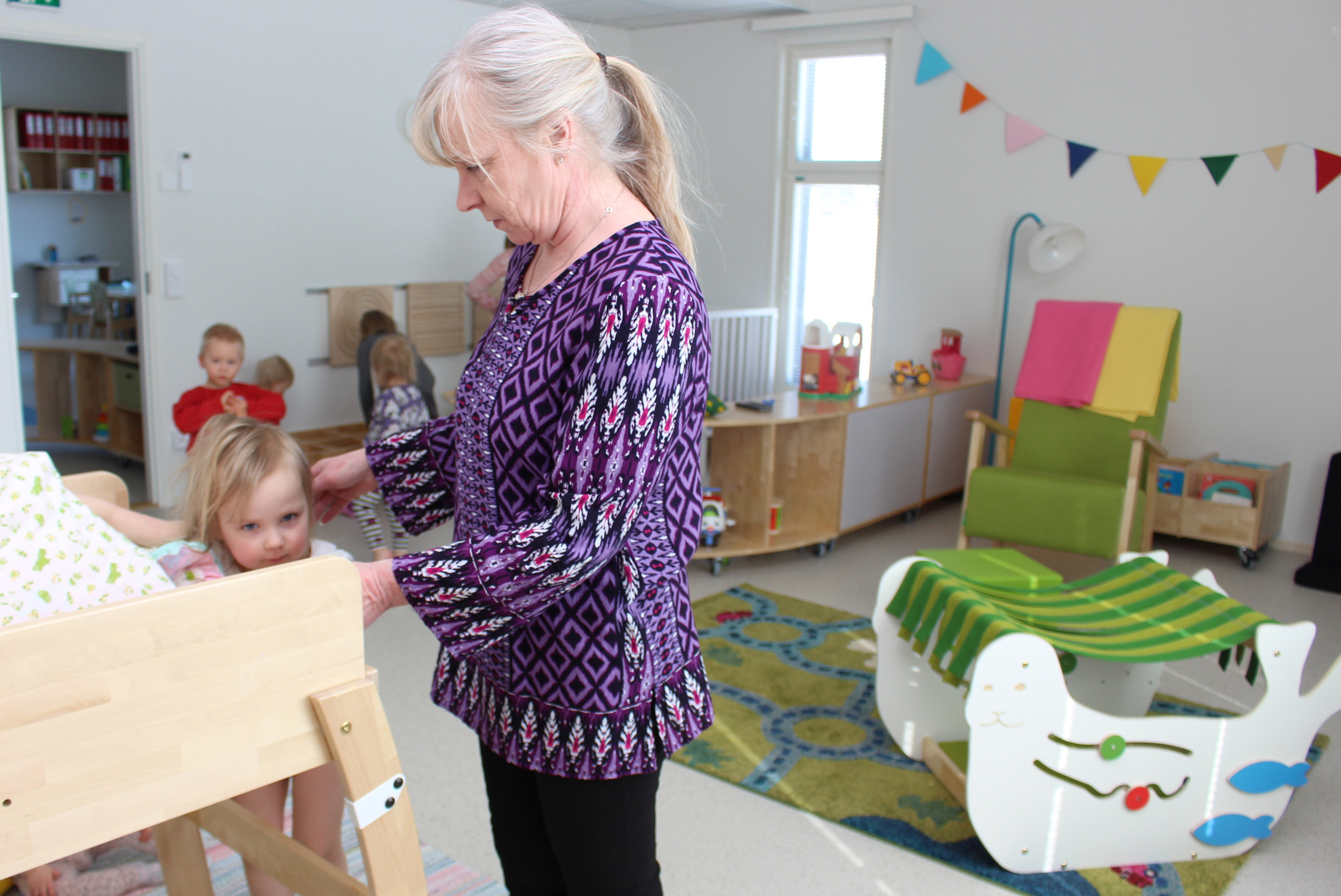 Pienimpien hoitolasten tiloissa Minttu heräillee viimeisenä päiväunilta. Kaverit ovat jo leikkimässä. Lastenhoitaja Heli Halmetoja varmistaa, että lapsi pääsee turvallisesti kaappisängystä alas.
