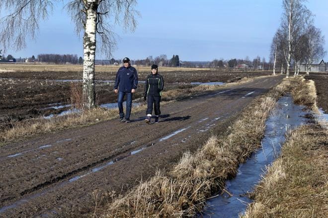 Tulvatilannetta tarkkailleet Maija ja Esa Huhtanen kävelevät kylätietä kohdalla, joka on normaalisti veden alla, kun vesi pääsetään Röyskölästä pellolle. Pienellä kummulla olevan tilakeskuksen tasalle tulva ei ole koskaan yltänyt ja tilalle johtava tie on ollut aina liikennöitävissä. Takana näkyvän painanteen paikalle Esa Huhtasen isä laski vuoden 1966 suurtulvan aikana verkot ja kalasti niillä hyvällä menestyksellä lahnoja. KUVAT: JOUKO HÄNNINEN