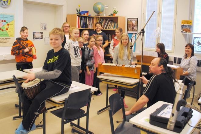 Petri Anttila asensi mikrofoneja paikoilleen, kun bändikerholaiset opettajansa Paula Männikön johdolla availivat ääniään. KUVA: EEVA-LIISA KULJU