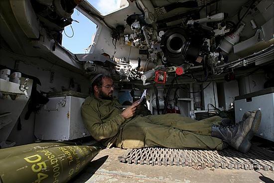 Tykkimies lueskeli ajankulukseen 155 millimetrin kranaattien vieressä Israelin telakanuunan sisällä tulitauon astuttua voimaan varhain maanantaina.