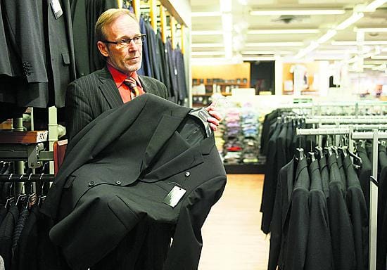 Sisäänostaja Kari Koivunen pitelee käsessään yksirivistä ja kaksinappista pukua, joka on valmistettu nanokankaasta. Puku hylkii vettä ja likaa.