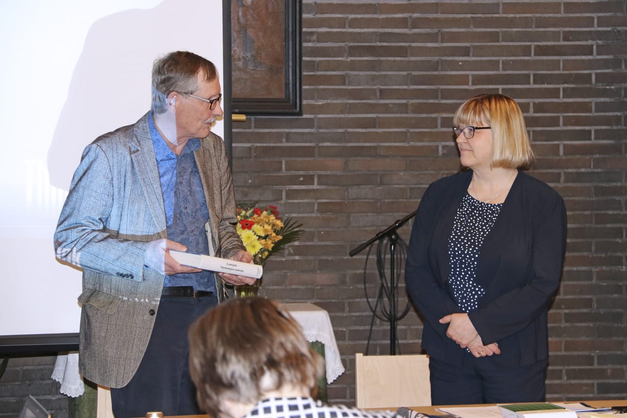 Eino Jakkula ojensi Paula Karsi-Ruokolaiselle tuhdin paketin iltalukemista Lumijoen kotiseutukirjan muodossa.