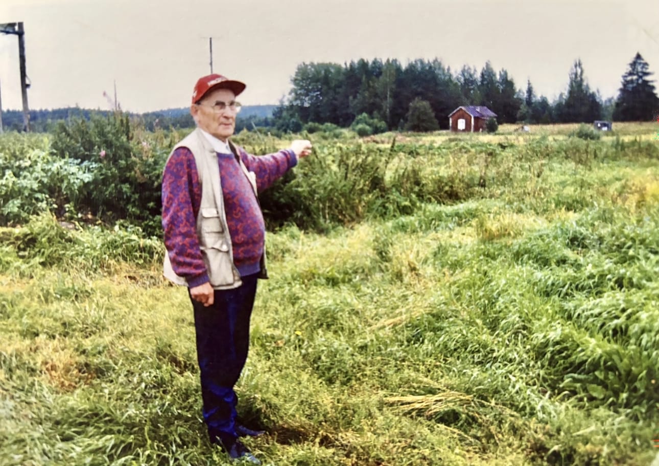 Lauri Halla-aho viittilöi kohti vanhan kotinsa paikkaa Hoiskon Halla-ahossa. Taustalla näkyy hänen tätinsä Hilma Ojajärven perheen koti. Kuva on otettu todennäköisesti vuonna 2000.