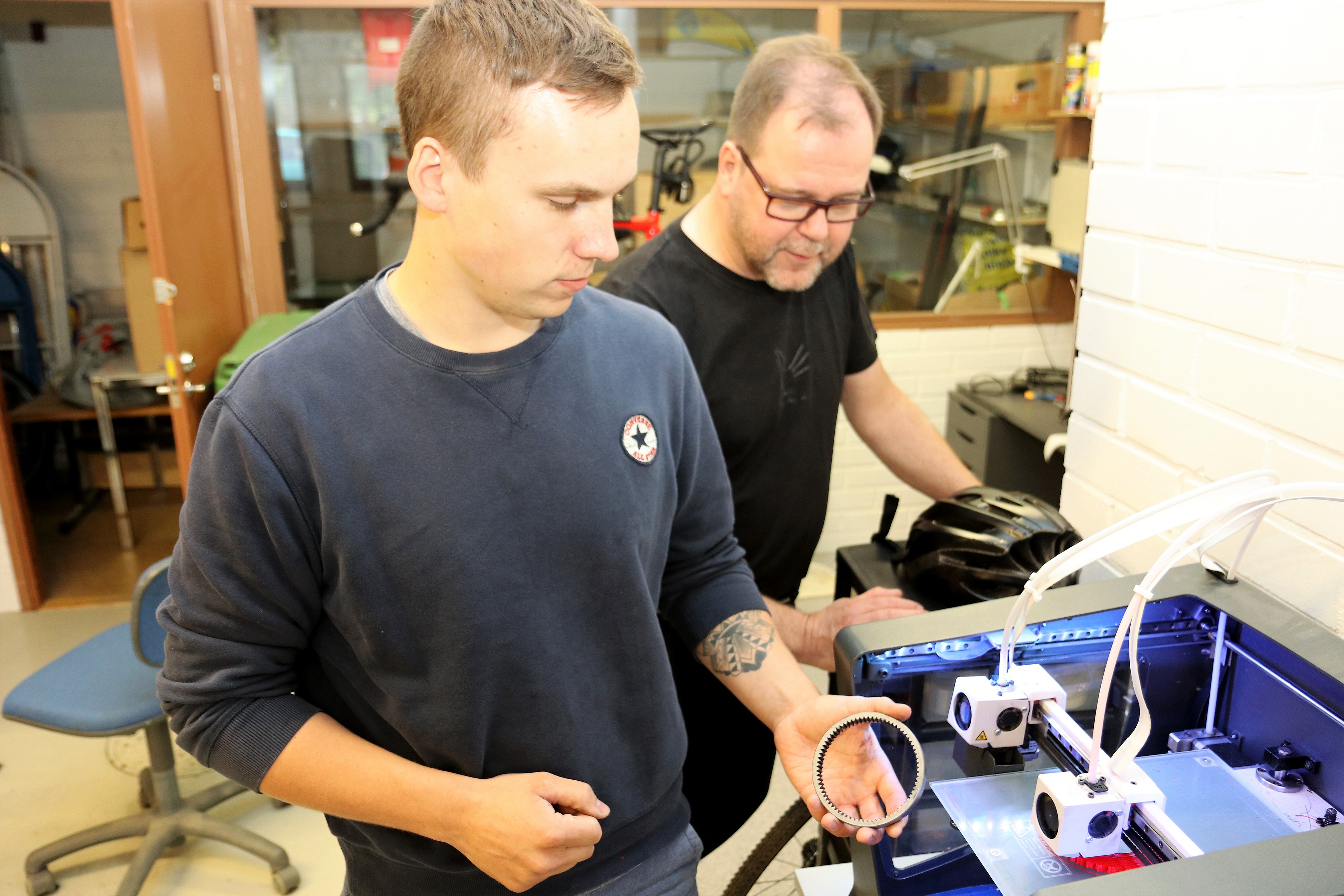 Iiro Peltola (edessä) ja Antero Jalkanen valmistelevat sähköpyöräilyn vallankumousta. 3D-printteristä on valmistumassa moottorin rattaan prototyyppi.