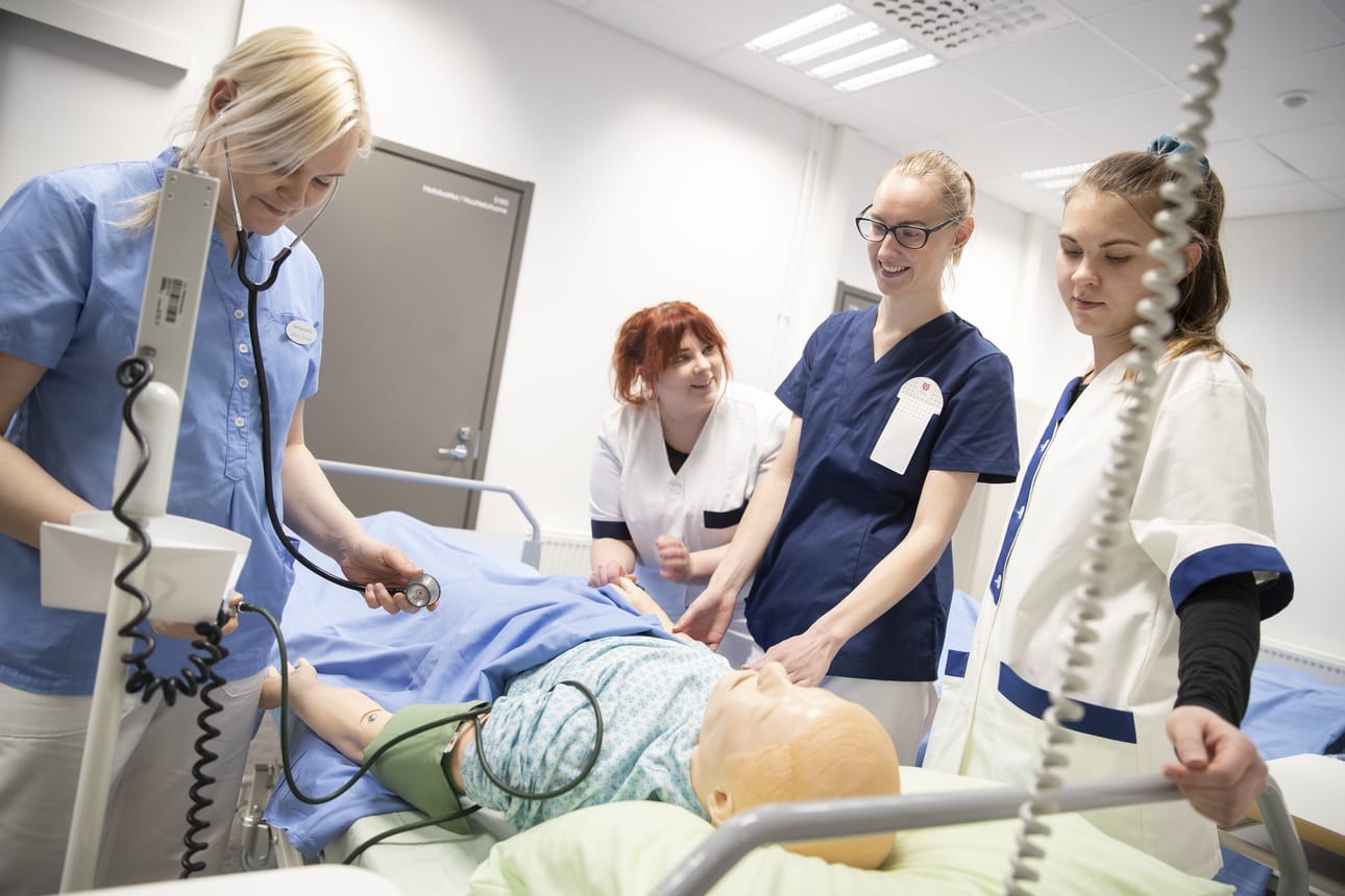Lähihoitajaksi opiskelevat Johanna Stenroos (vasemmalla), Kamilla Lehtonen, Henna-Sofia Pohjola ja Nella Agge harjoittelevat hoitotoimia nuken kanssa.