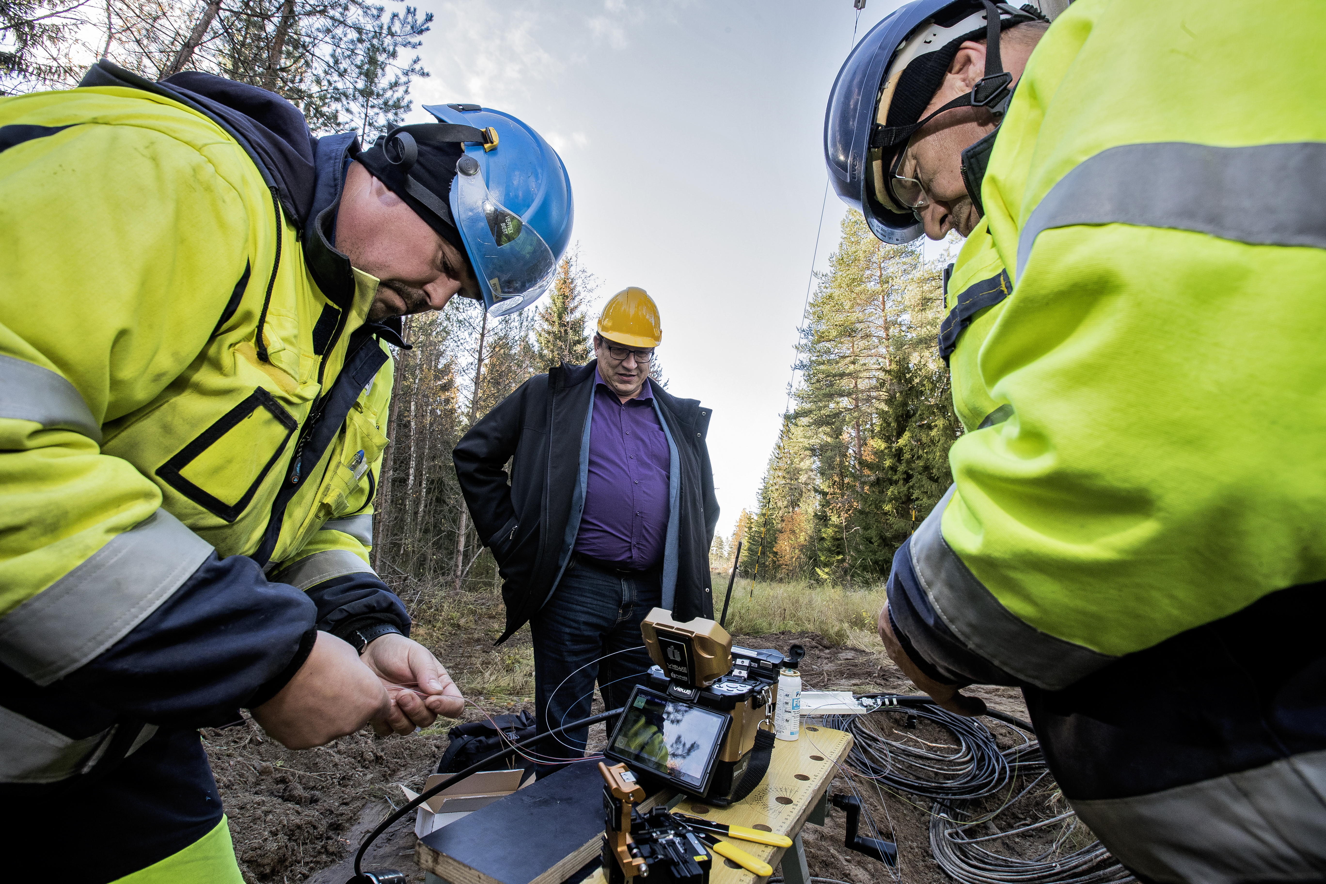 Raahen Energian verkostoasentaja Petri Salin ja verkostotyöntekijä Pekka Tuomaala hitsaavat valokuitua Hiihtomajan lähistöllä kannettavalla kuituhitsauskoneella. Toimitusjohtaja Lasse Lahti (keskellä) toivoo, että vastaavia töitä tehtäisiin lähivuosina Raahessa runsaasti.