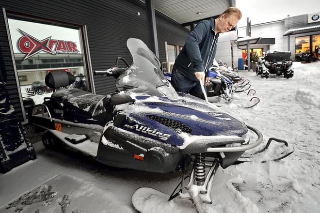 Myyjä Hannu Kuusela putsaa moottorikelkkoja yöllä sataneen lumen alta. Kuusela toivoo tulevilta päiviltä suojasäätä, jolloin kelkkareitit saataisiin ajettua. KUVA: HEIKKI HAKANEN