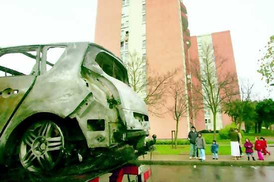 Tornitalojen varjo. Nuorisojoukkojen polttamaa autoa siirrettiin kadulta Trappesin esikaupunkialueella Pariisissa perjantaina.