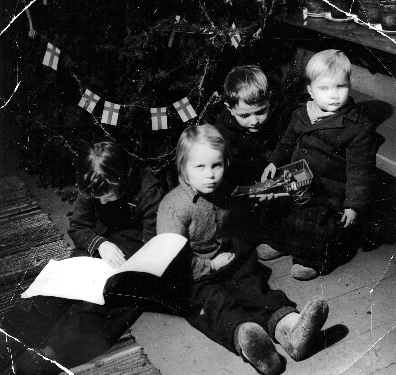 Joulutarinan kirjoittaja, vaaleahiuksinen Matti Pietarila (oik.) istuu joulukuusen äärellä lapsuudenkodissaan Pudasjärven Kurenalla vuonna 1954. Vieressä istuu Erkki-veli, Paula-sisko on syventynyt lukemaan. Kameraan katsoo naapurista vieraisille tullut Leena-tyttö.