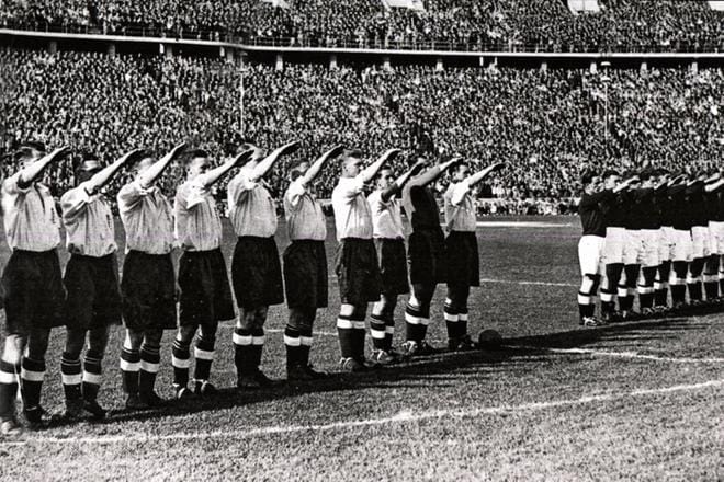 Erittäin vastahakoinen Englannin jalkapallomaajoukkue (vas.) määrättiin tekemään natsitervehdys Berliinin stadionilla ennen ottelua isäntämaa Saksaa vastaan vuoden 1936 olympiakisoissa. Englanti voitti pelin maalein 6–3. KUVITUSTA KIRJAAN PALLON HERRUUS.