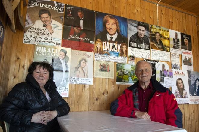 Tähtien keskellä. Riitta Schwöbel ja Simo Seppälä istahtivat pöytään, jonka takana seinällä komeilee Vehu-talossa konserttinsa pitäneitä laulajia. Kylätalon viereen on valmistunut myös iso grillikota. KUVAT: JARI KARJANMAA