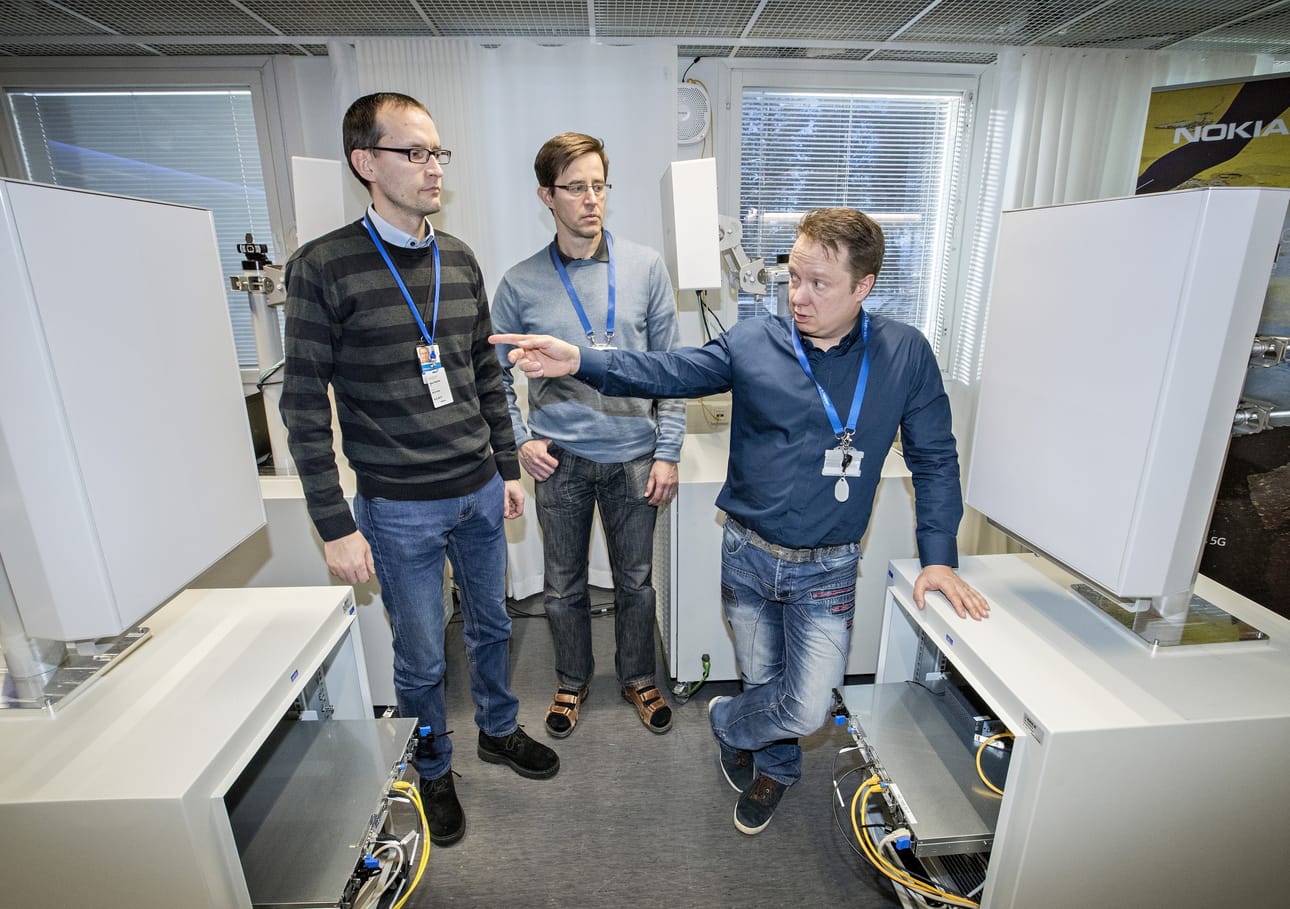 Nokian 5G-ohjelmajohtaja Aki Korvala (oik.), yliopiston 5G-projektipäällikkö Olli Liinamaa ja VTT:n projektipäällikkö Atso Hekkala toimivan 5G-demolaitteiston välissä. Näissä laitteissa on näkyvillä Nokian useiden vuosien työt 5G:n parissa alkaen vuoden 2011 ensimmäisistä patenteista.