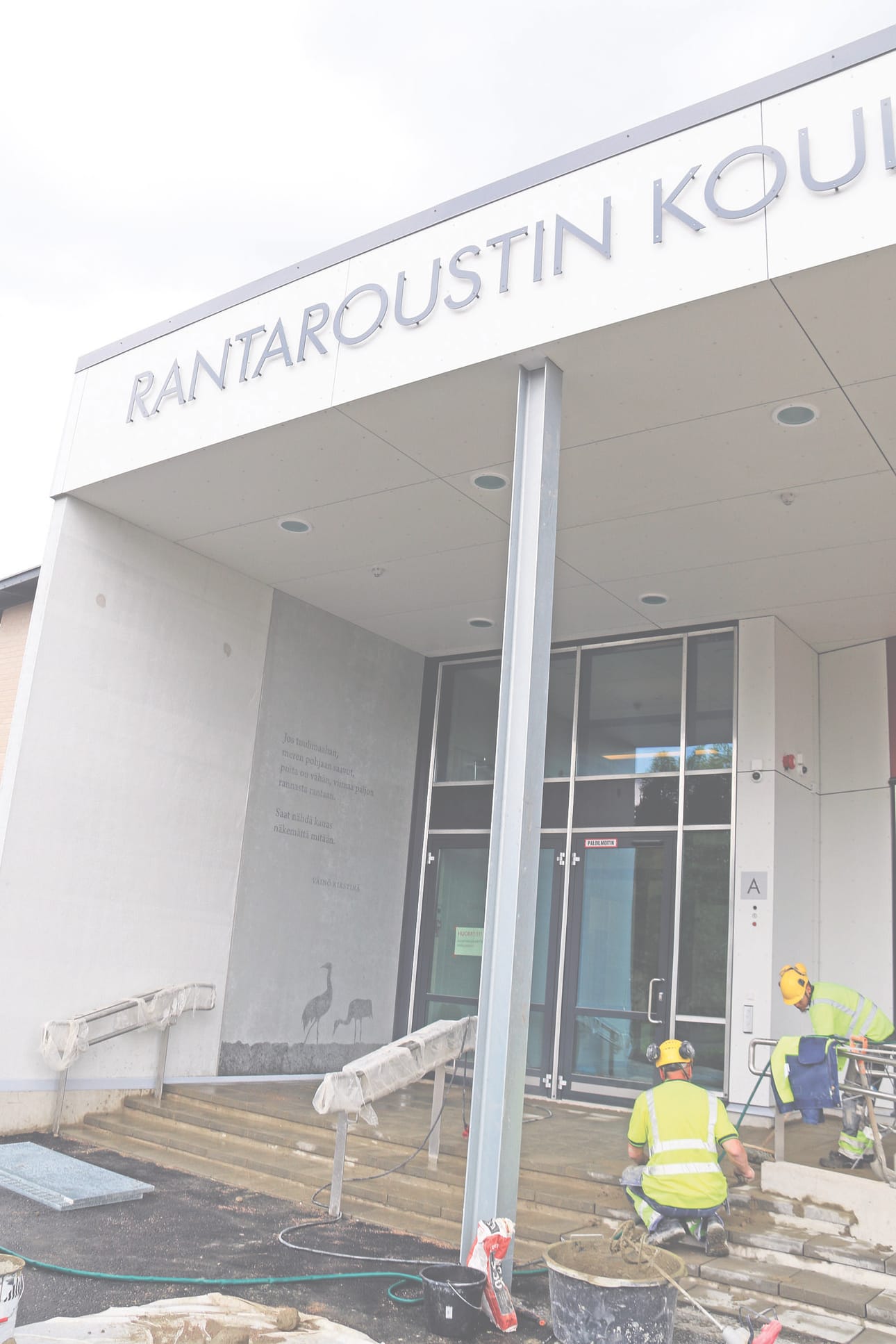 Koulun pääsisäänkäynti. Vasemmalla Väinö Kirstinän runo seinään ikuistettuna.