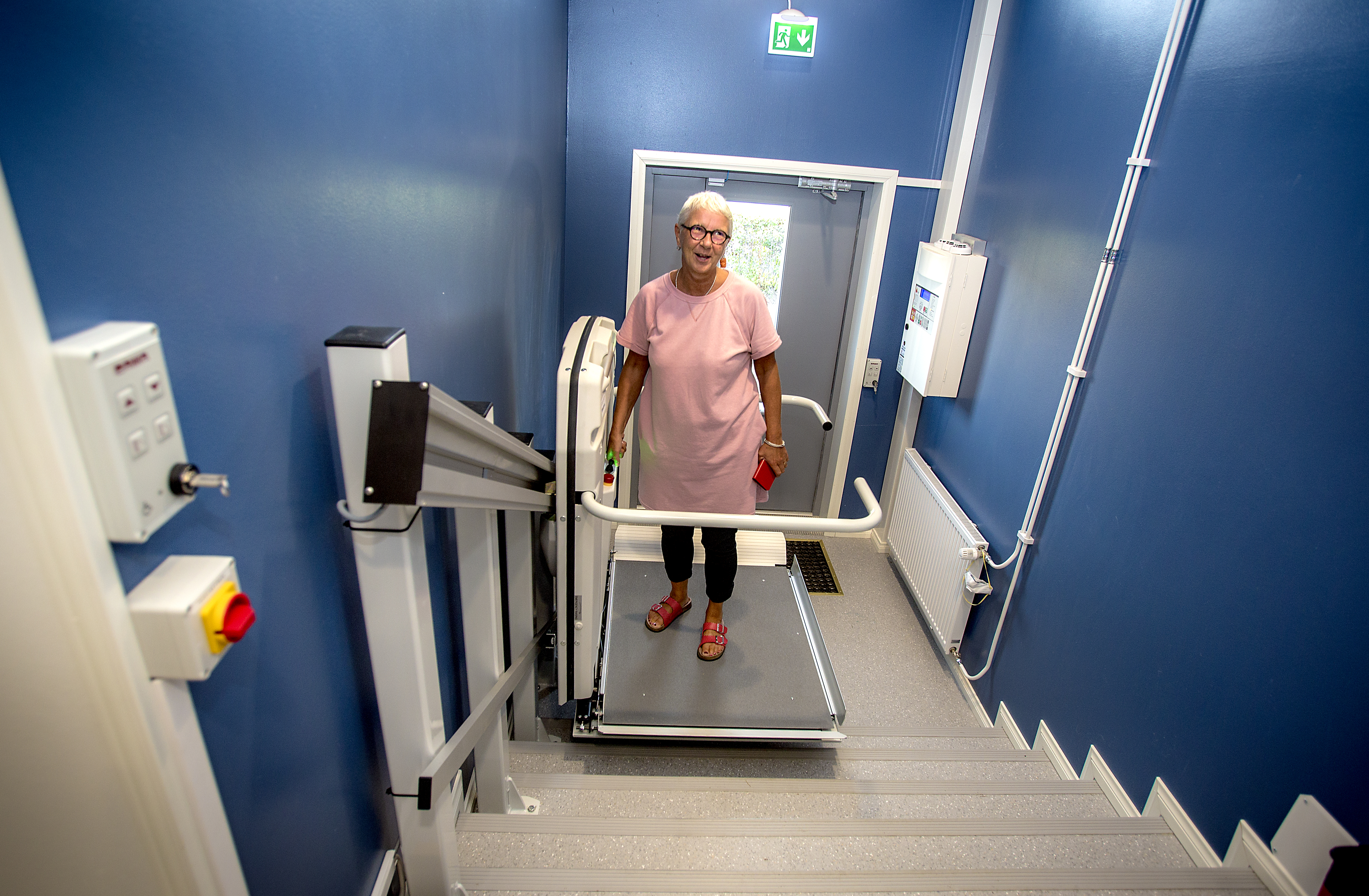 Asiakkaita varten talon etuovella on invalidihissi. Pyörätuolilla mennään lavalle, joka siirtää asiakkaan ensimmäiseen kerokseen. Sitä käyttöä demonstroimassa Kaisu Kaasalainen juuri niin kuin sitä ei koskaan pitäisi käyttää: ilman pyörätuolia.