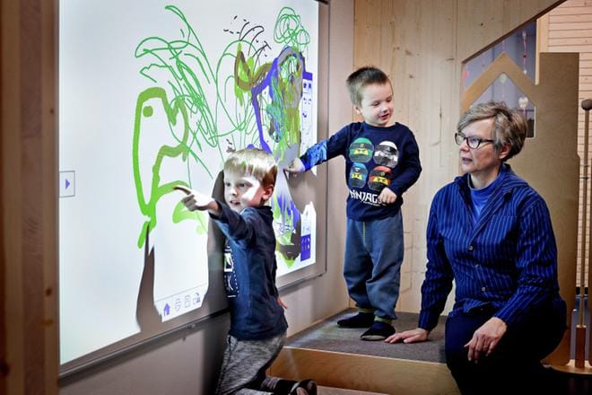 Eeli, 5, ja Rami, 4, tulkitsevat Taika-päiväkodin johtajalle Tarja Louhirannalle piirrostensa syvintä olemusta. Taiteilijoiden työskentelyalustana on kosketusnäytöllä varustettu älytaulu seinäjokelaisen päiväkodin seinällä. KUVA: KARI LÖFHJELM