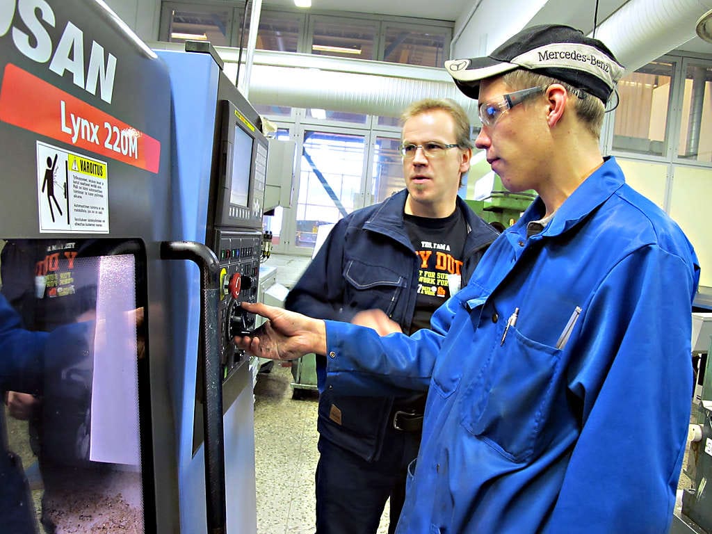 Nivalan ammattiopiston metallilinjalla toista vuotta opiskeleva Matti Meriläinen (oik.) valmistelee tässä pinnapultin sorvaamista CNC-sorvilla opettajansa Pasi Hautamäen opastamana.