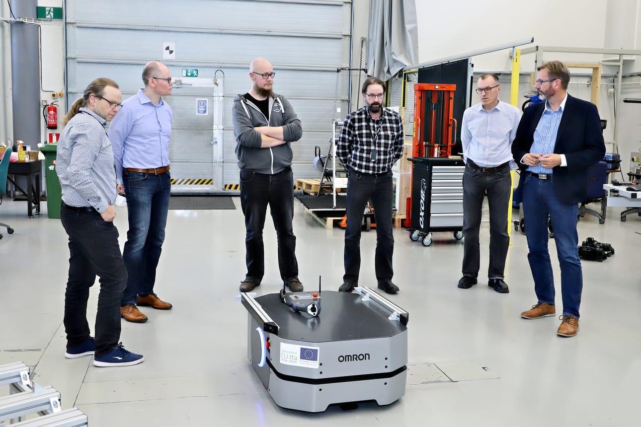 Centrian robotiikkalaboratorio on lehtori Jari Kaarelan (vas.), TKI-kehittäjä Sami Sarlinin ja lehtori Tero Kaarlelan (kesk.) työympäristö. He kertovat Tommi Sirviölle, Risto Rovalle ja Sampo Siikille, että teollisuuden käytössä olevaa mobiilirobottia pystytään hyödyntämään myös akkujen kierrätysteollisuuden tarpeisiin.