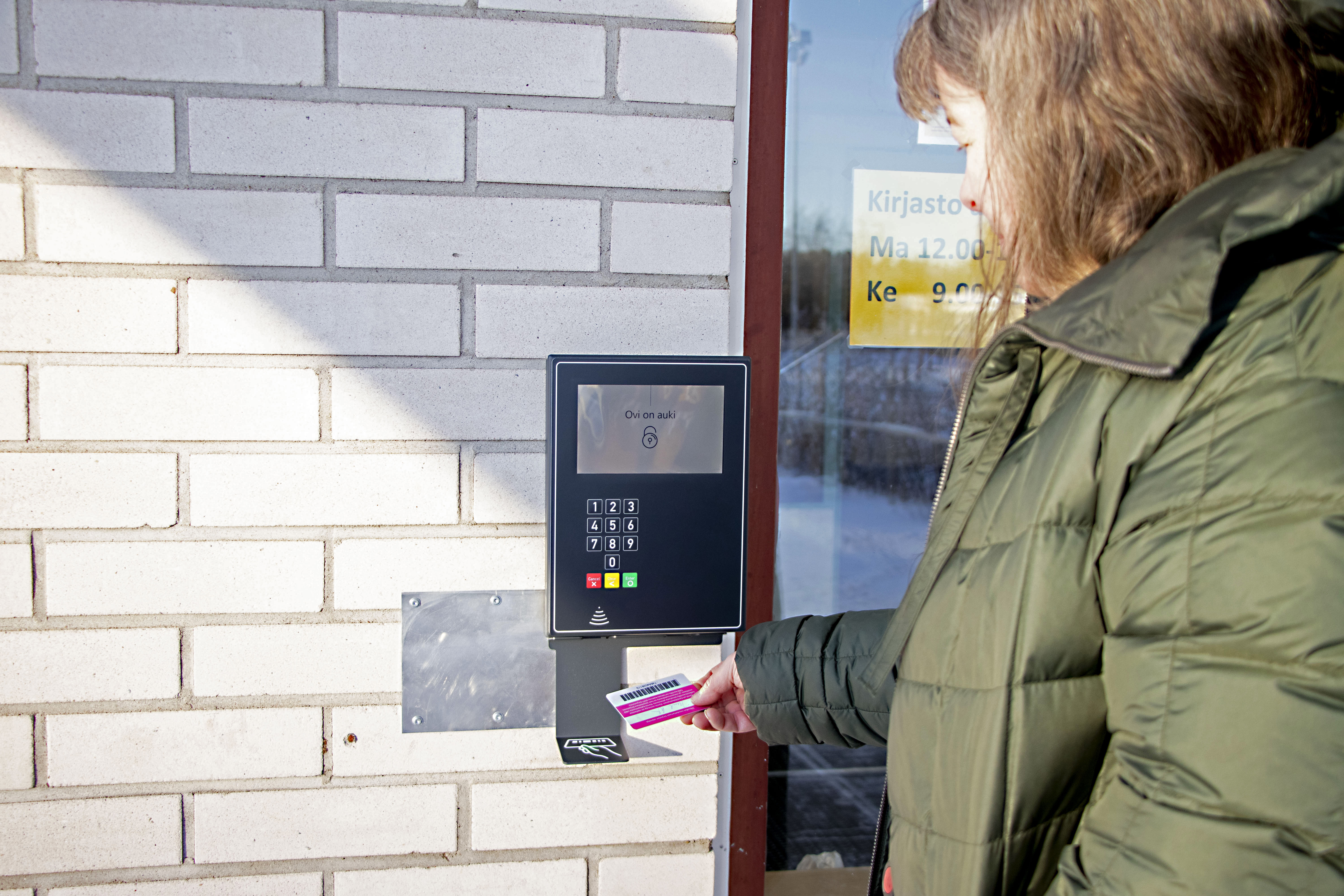 Tuula Kuoppamäki näyttää, kuinka kirjastokortin viivakoodia vilautetaan kirjautumisyksikölle.