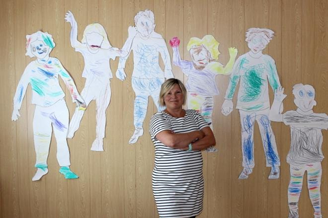 Työ päiväkodissa antaa vapauden olla luova. Mia Jokisen taustalla on 3-5-vuotiaiden hoitolasten eli mustekalojen tekemiä omakuvia. KUVA: MINNA ZILLIACUS
