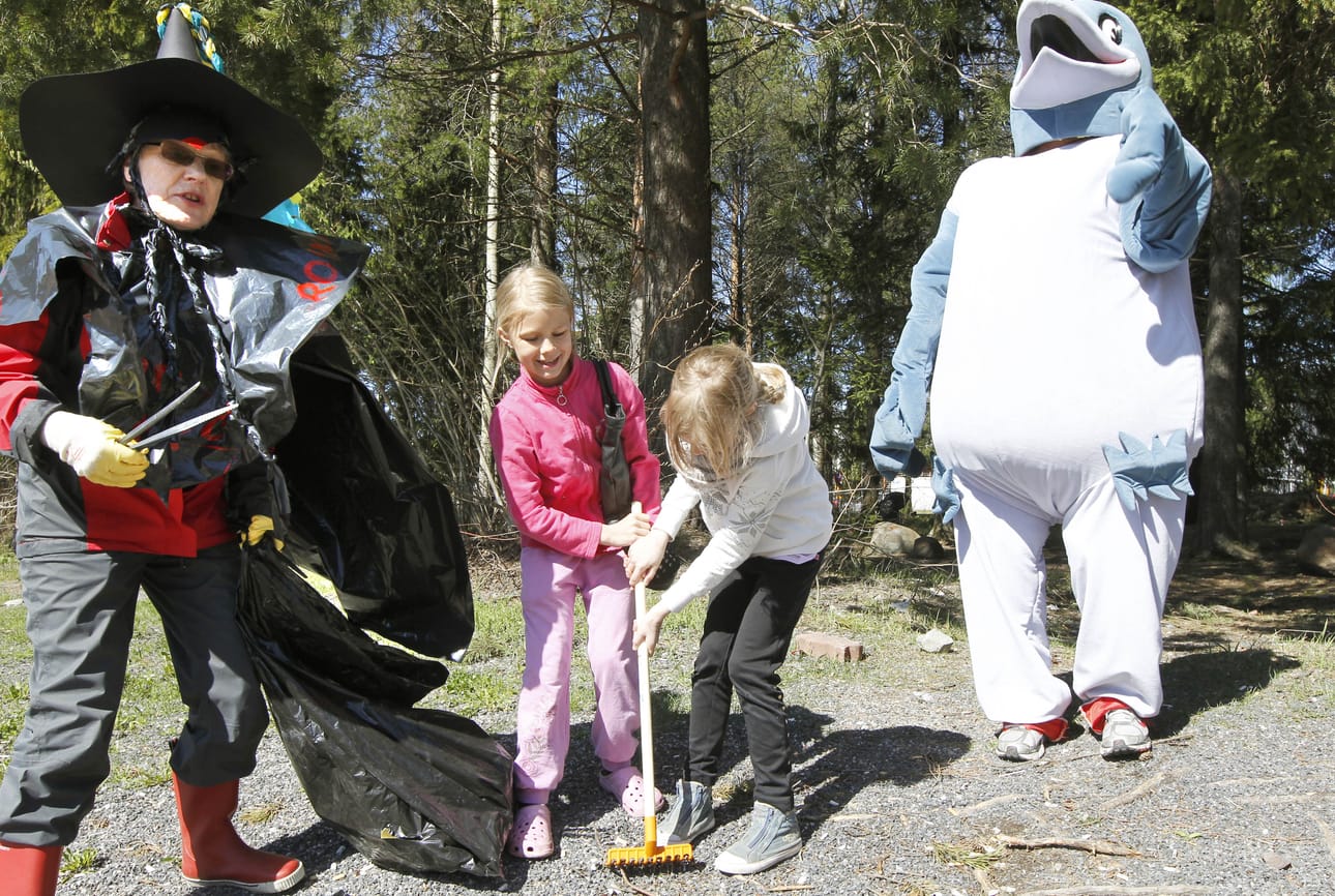 Oiva Roina -varis valvoo kun 8-vuotiaat Janika Kuukasjärvi (oikealla) ja Julia Siipola opettelevat haravoimaan roskia pois ympäristöperformantikko Leena Niirasen avustuksella.