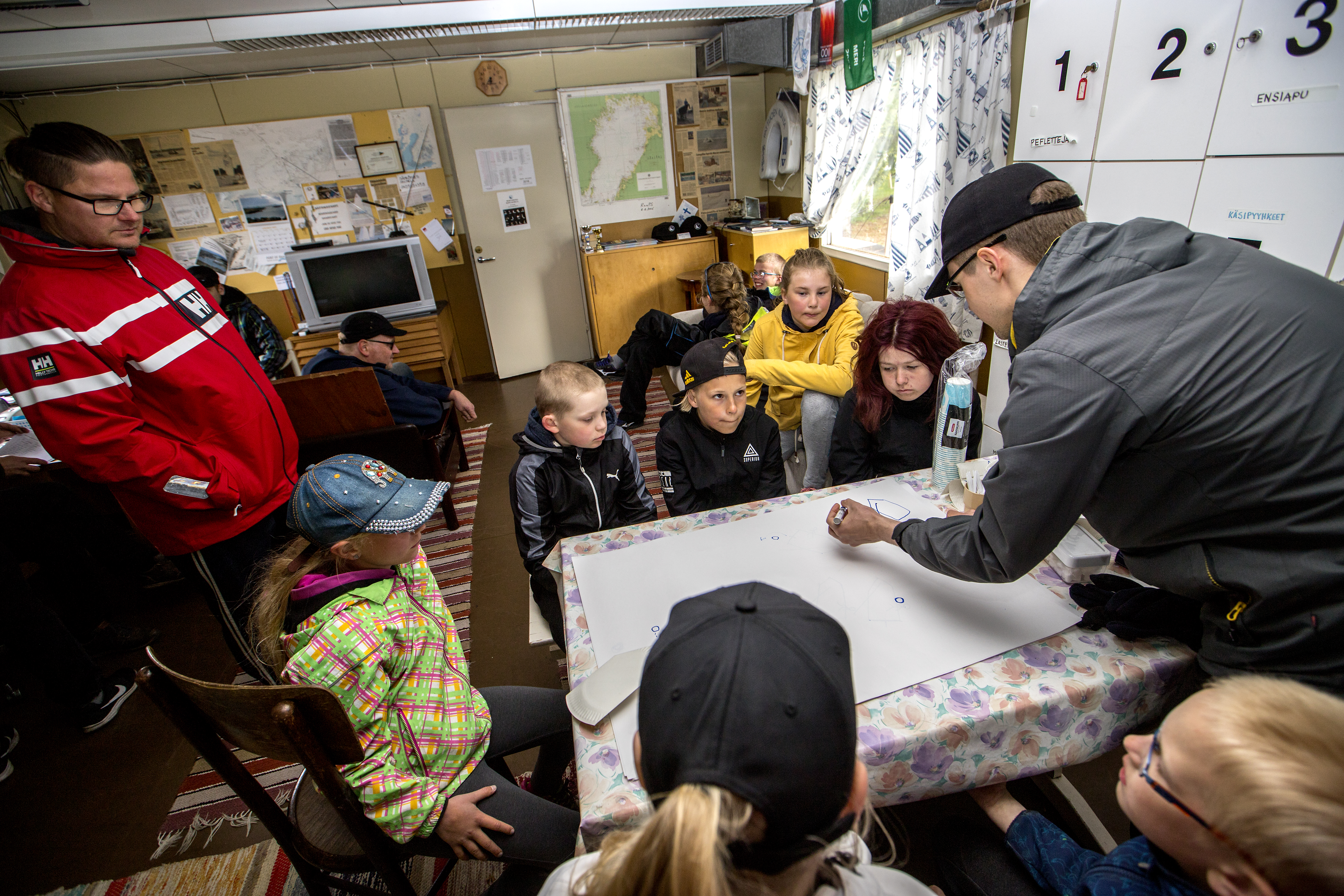 Raahen Purjehdusseura kouluttaa lapsia purjehtimaan. Mikko Sipola kertoo pöydän ääressä, miten vastatuuleen luovitaan.