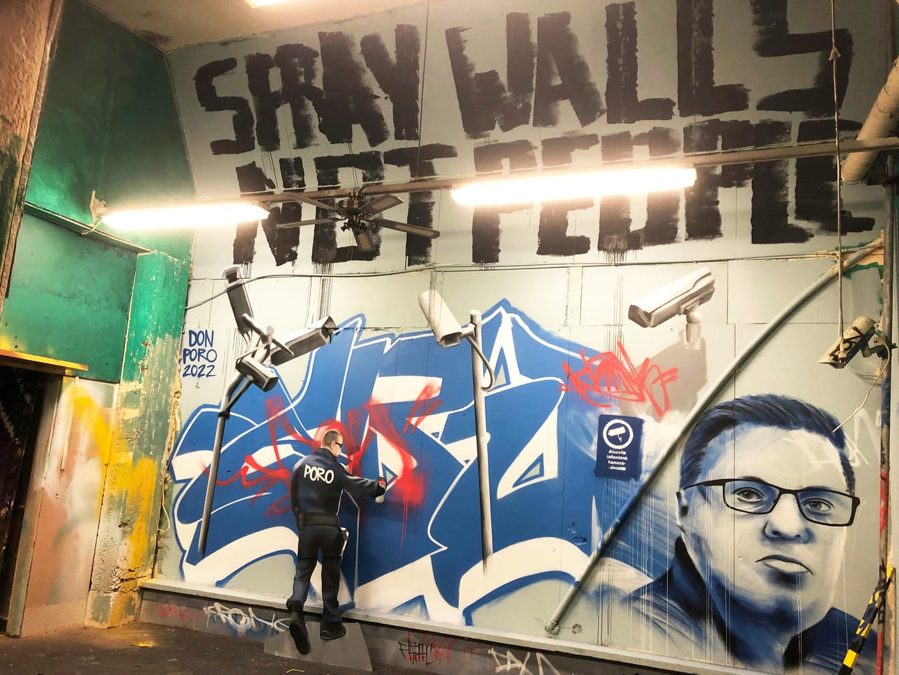 Sumuta seiniä, älä ihmisiä. Taiteilija maalasi tämän työn kommenttina pari vuotta vanhaan tapaukseen, jossa poliisi sumutti kadulla istuneita mielenosoittajia.