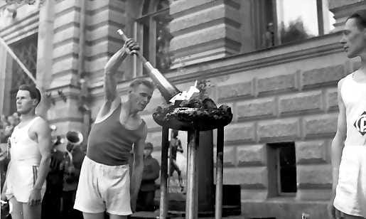Olympiatuli matkalla. Entinen olympiamies Niilo Hartikka ottamassa tulta olympiasoihtuun Oulun kaupungintalon edustalla 9.7.1952.