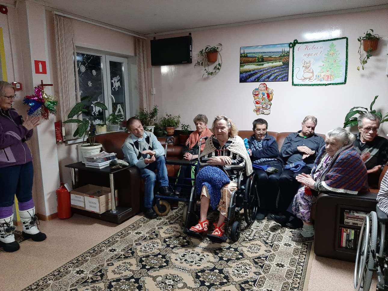 Osa Kalevalan vanhaintalon vanhuksista taputtaa käsiään ohjelmanumeronsa esittämisen jälkeen. Kuvan vasemmassa reunassa Paula Rainaho. Naisilla on hartioillaan uutukaiset saalit. Miehet saivat sukkia ja muuta lämpimäistä. Kaikille oli tiedossa suomalaiset kahvit ja paikallisesta kaupasta ostetut appelsiinit.