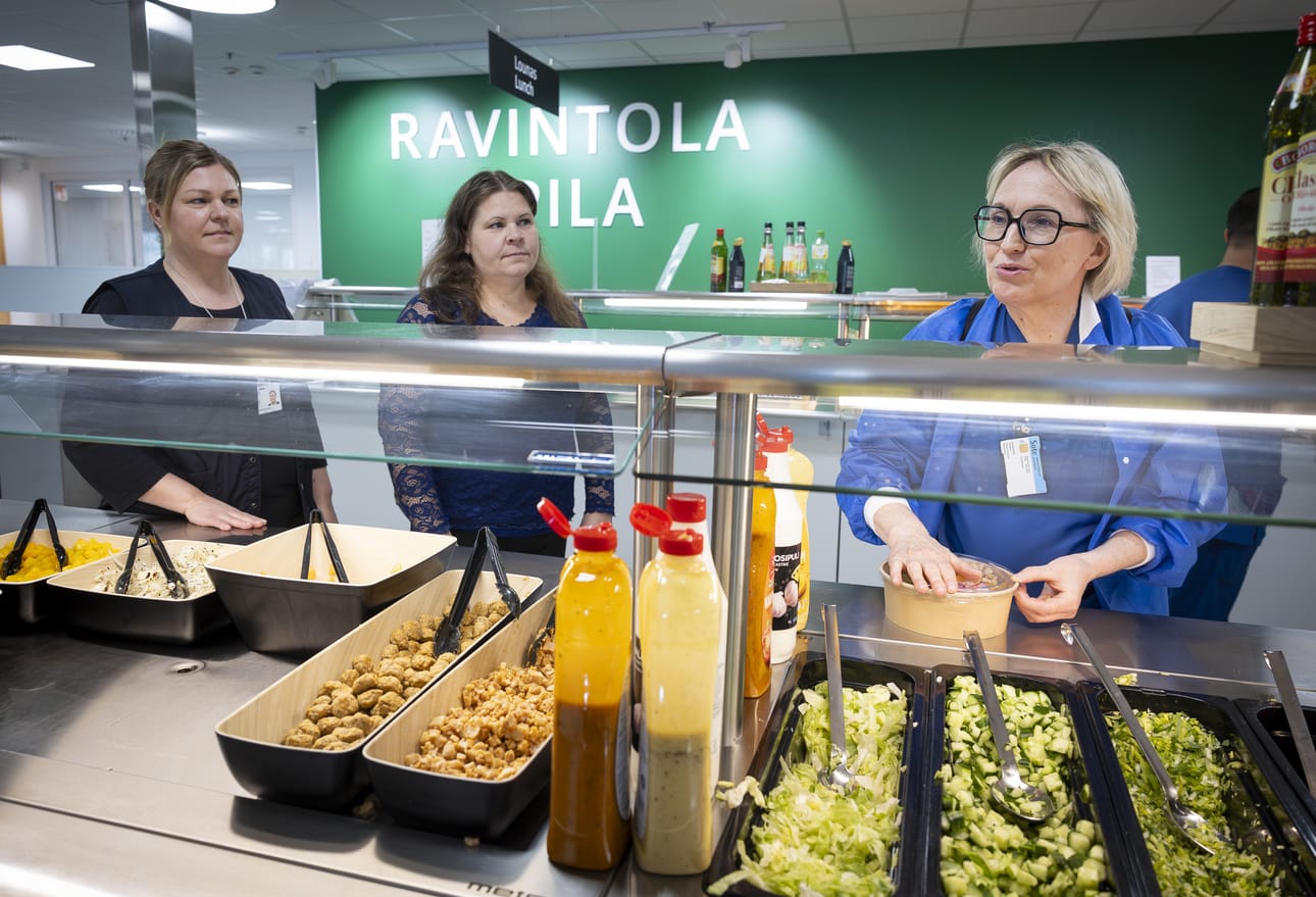 Ravintola Apilan ruokapalveluvastaava Anu Saarenpää (vas.), Pohteen ateria- ja puhtauspalvelujohtaja Tanja Koski sekä päivän lounaan noutanut Kristiina Kumpulainen lounaslinjaston äärellä.