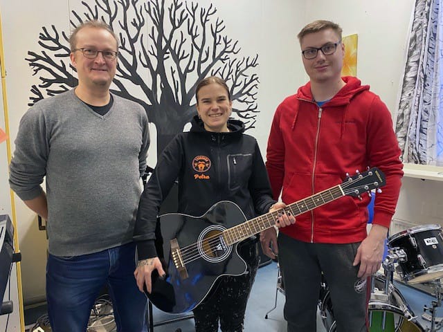 Kuvassa Mikko Kukkohovi (vasemmalla) luovuttaa kitaran Tyrnävän kunnan nuorisotoimen edustaja Petra Särkelälle sekä bänditilan käyttäjiä edustajvalle Ville Turuselle.