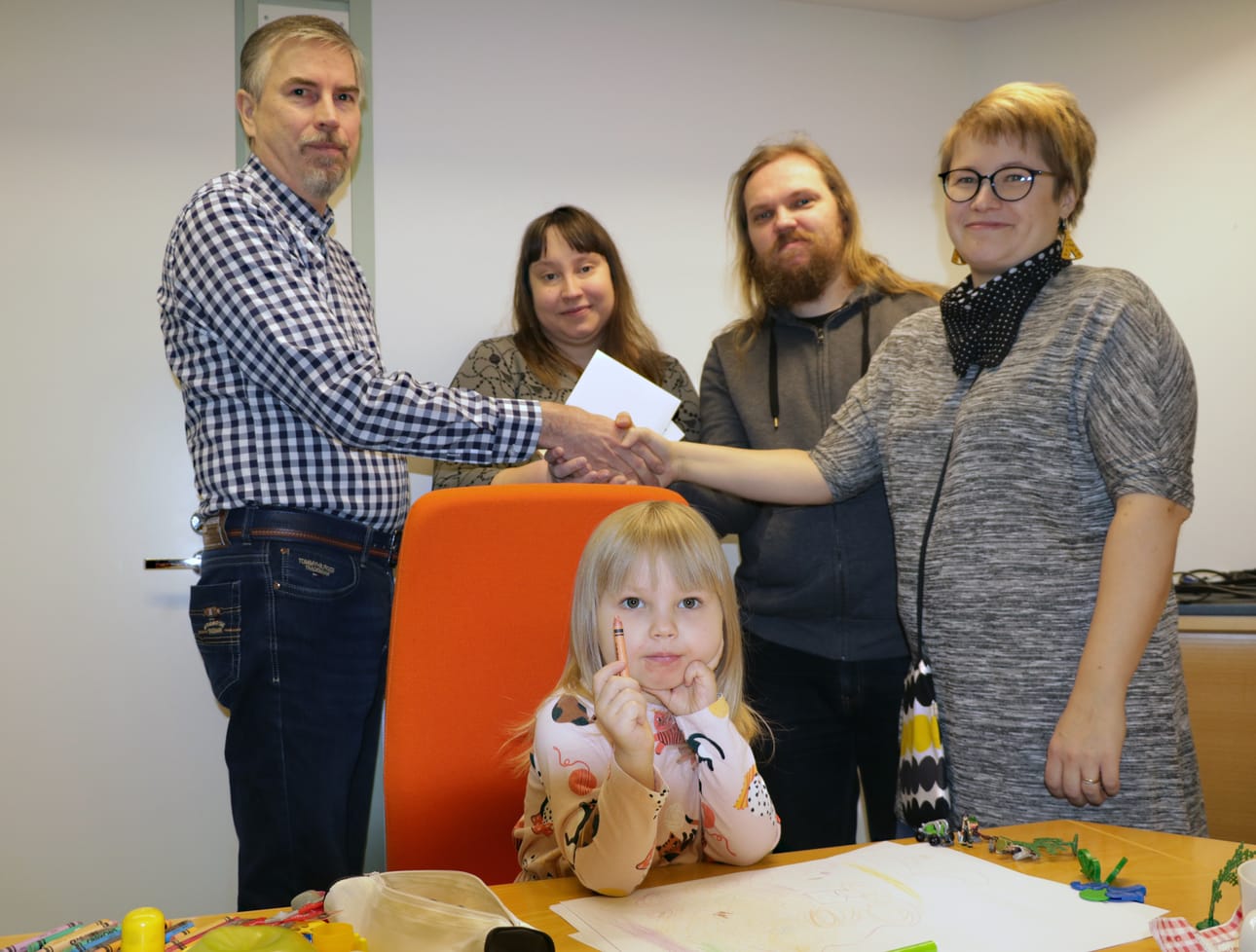 Pyhäjokiseutu-lehti muisti paikallista MLL:n yhdistystä joulutervehdyksistä saaduilla euroilla. Tuhannen euron lahjoitusta antamassa Matti Torvi (vas.), vastaanottamassa Satu ja Samuli Tikkanen sekä Reeta Isola. Etualalla piirtämässä Pihla Tikkanen.