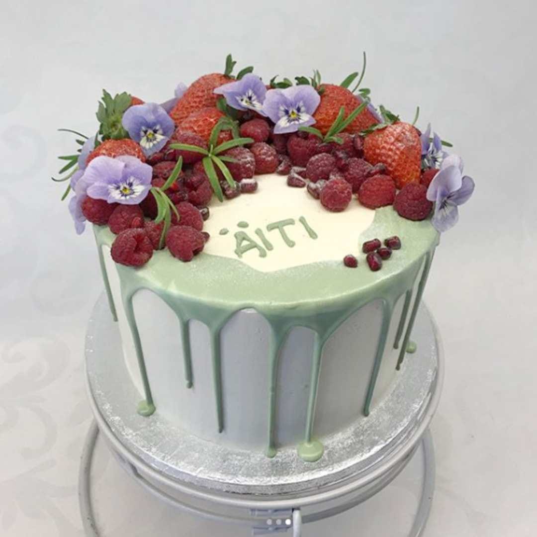 Ajan hermolla. Näyttävän valuva drip cake on saanut pinnalleen tuoreita marjoja ja syötäviä orvokkeja.