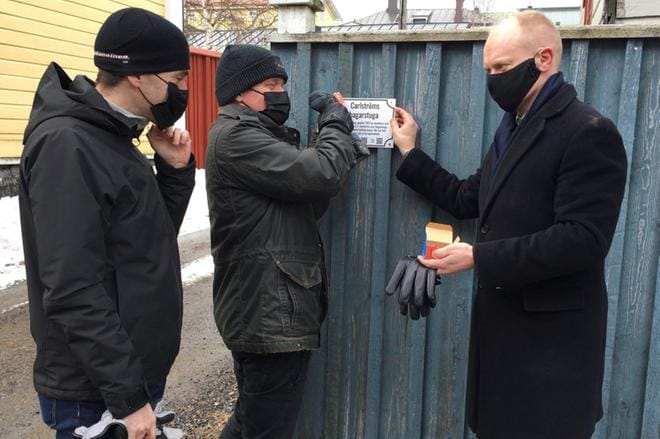 Dag Björklund seuraa, että kyltti tulee suoraan. Tommi Haapanen ruuvaa ja Harri Alatalo pitää kylttiä paikoillaan. Testikyltit ovat sillä kielellä, jolla talonomistajat ovat tekstin antaneet. KUVA: SEPPO KUUSINEN