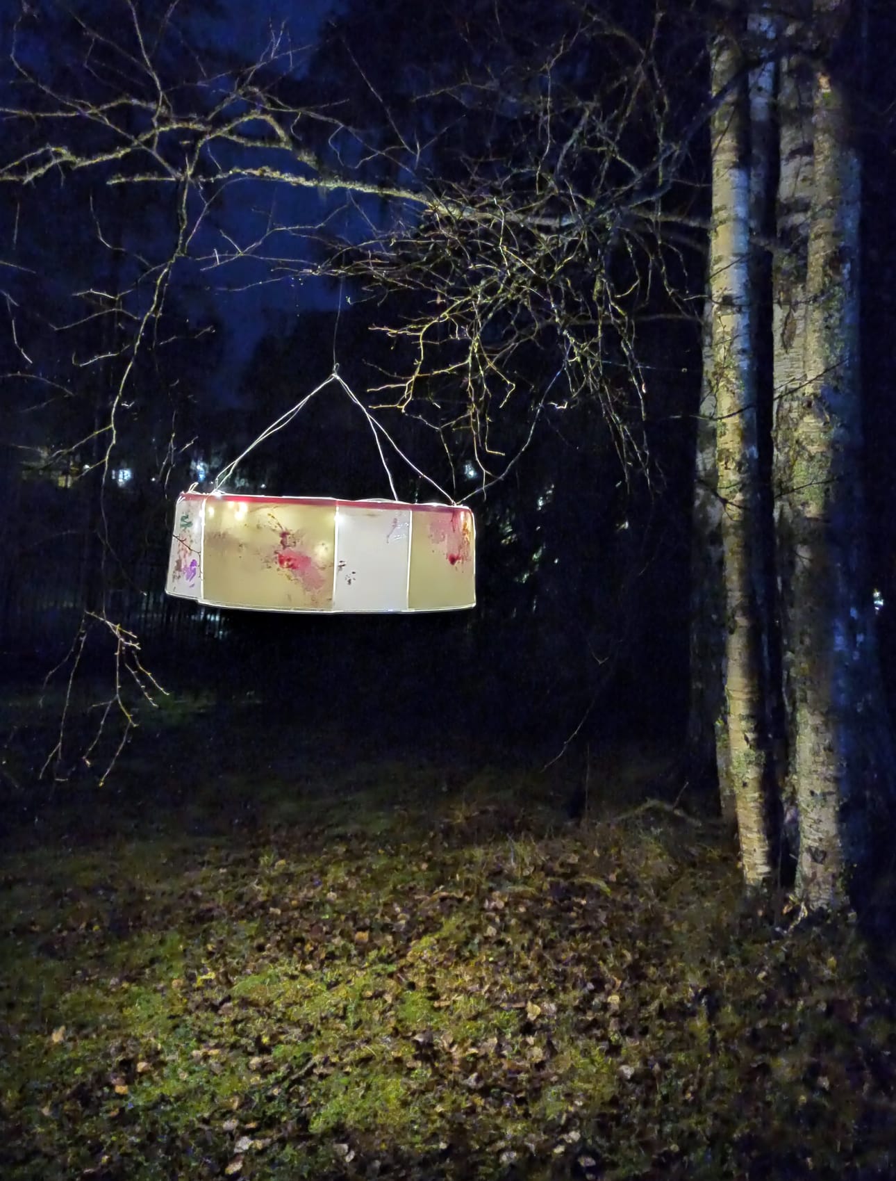 Koivun oksalla riippuvati MLL:n perhekahvilan vauvojen ja taaperoiden väritykset, jotka oli koottu kauniiksi varjostimeksi.