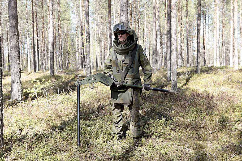 Yliluutnantti Petri Junttila etsi räjähteitä Pudasjärvellä metallin ilmaisevalla syväetsimellä. Se löytää metallin syvemmältä kuin miinaharava. Raivaajilla on yllään yli 20 kiloa painava raivauspuku. Tauko pidetään 20 minuutin välein.