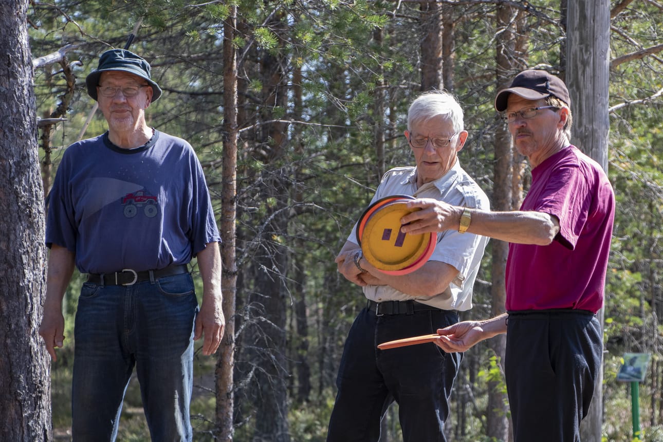 Jouko Taipaleenmäki (oik.) opasti Tapani Alasalmea ja muuta väkeä frisbeegolfin saloihin. Matti Leinoselle laji on jo tuttu ja miehen mukana olikin repullinen heittovälineitä.
