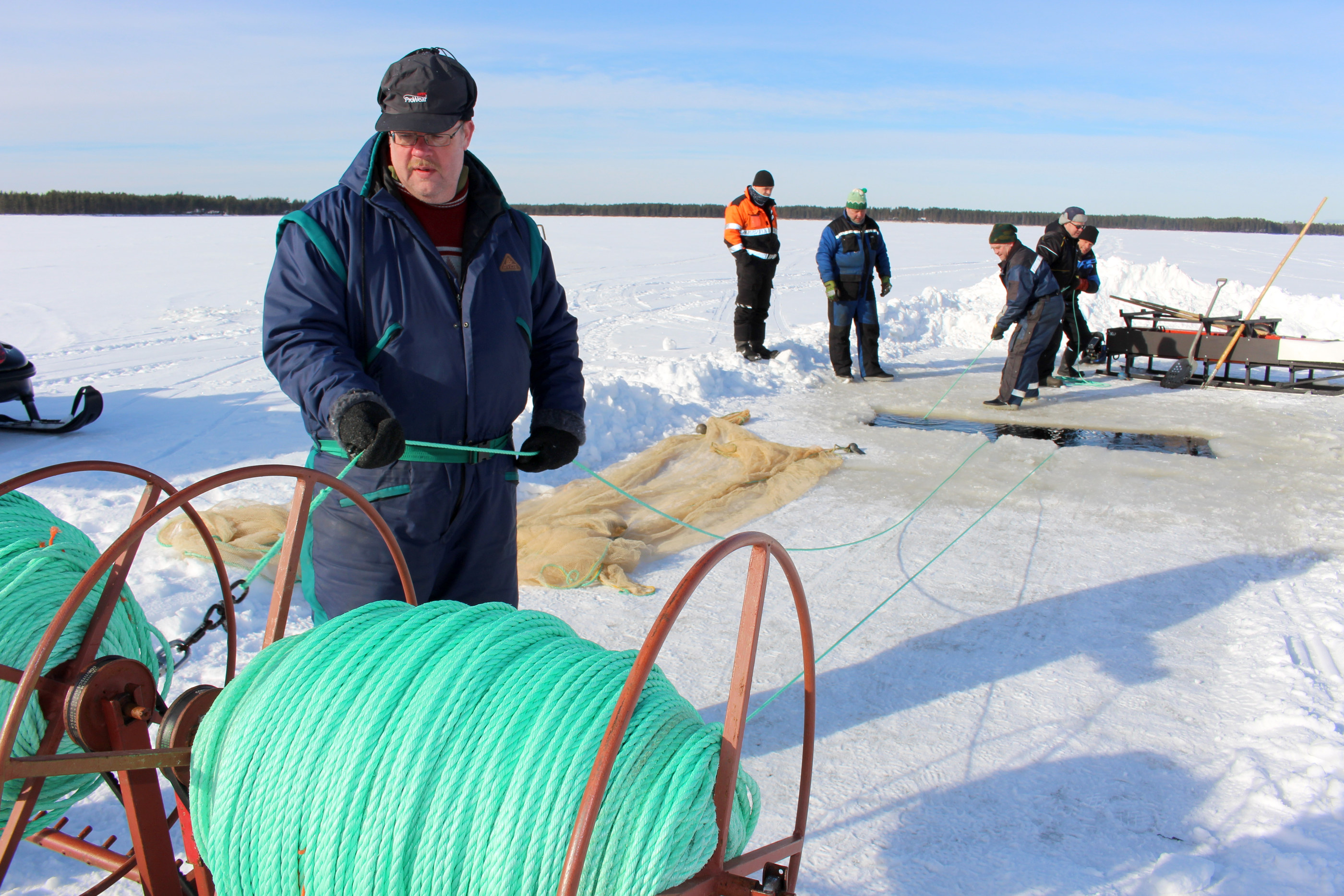 Pekka Piippo varmistaa, että nuotan vetoköydet ohjautuvat kelalle tasaisesti. Taustalla nuottaa kiskovat Timo Pitkänen, Martti Luonua ja Jouko Koskelo, avannon reunalla kärsämäkiset Ilpo Vattu ja Reijo Kallinen
