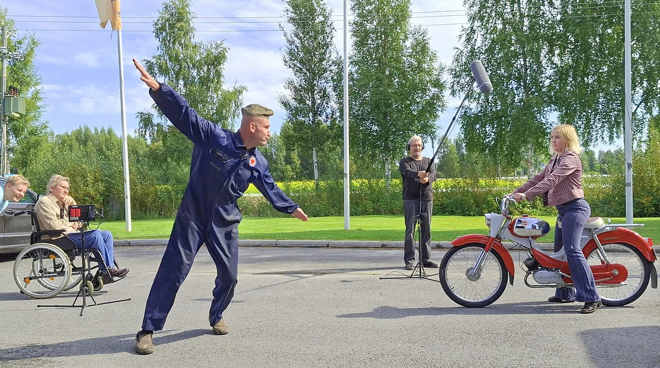 Jugoslavialainen Kreso (Tero Hurtamo) vaikuttaa kuvailevan lentokoneen liikettä nuorelle Lempille (Laura Jokinen. Kuvaaja Pekka Pohjoispää ja Jukka Mäkinen seuraavat, kuinka kohtaus sujuu. Jarmo Kumpula ottaa ääntä talteen.