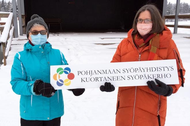 Eila Kuusisto ja Kaija Kiviluoma pitelevät kädessään kuortanelaisen Markku Koivulahden teetättämää ja lahjoittamaa kylttiä. Kuvan on ottanut Rauno Mäki-Hallila.
