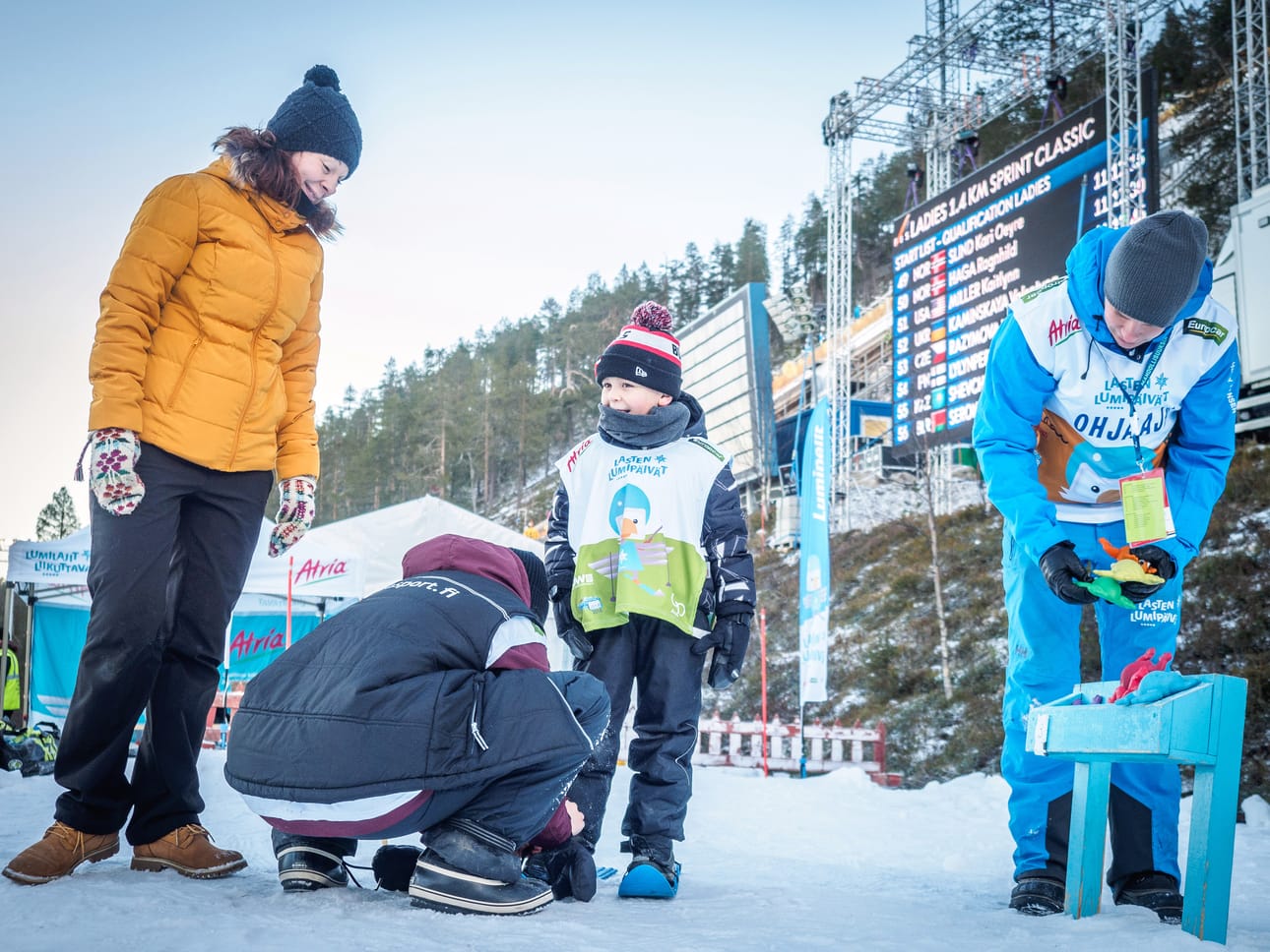 Niina Säippä katsoo, kun Otto Säippä, 5, saa minisukset jalkaansa Iris Lukkarilan avustamana. Henri Pelkonen asettelee kumisammakoita valmiiksi heittokisaa varten.